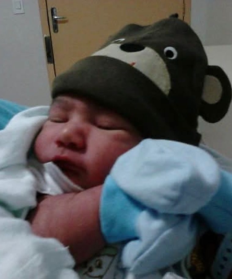 Dorah’s newborn son asleep in a brown monkey hat and blue mittens